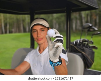 A woman proudly displaying a golf ball while seated in a golf cart on a lush green course during daylight hours - Powered by Shutterstock