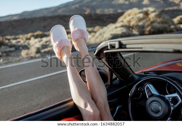 Woman pulling legs out of the car window on the\
roadside. feeling comfortable while traveling. Close-up on female\
legs in home slippers