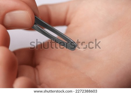 Woman pulling splinter from hand using tweezers on white background, closeup