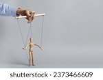 Woman pulling strings of puppet on light grey background, closeup. Space for text