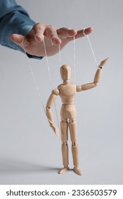 Woman pulling strings of puppet on light grey background, closeup