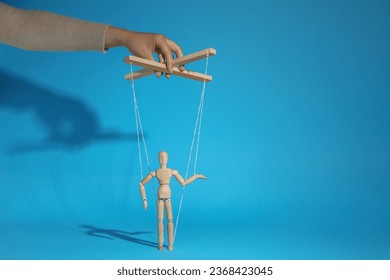 Woman pulling strings of puppet on light blue background, closeup