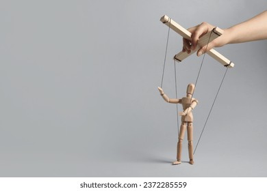Woman pulling strings of puppet on light grey background, closeup. Space for text