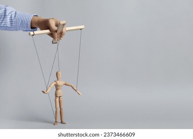 Woman pulling strings of puppet on light grey background, closeup. Space for text