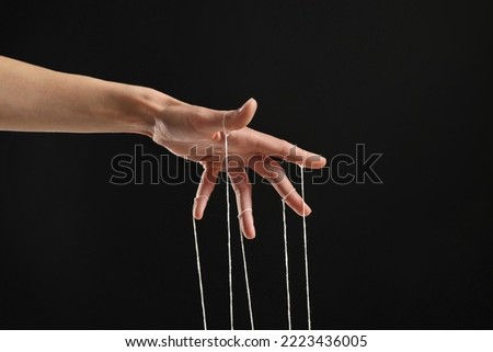 Woman pulling strings of puppet on black background, closeup