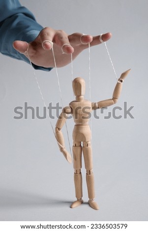 Woman pulling strings of puppet on light grey background, closeup