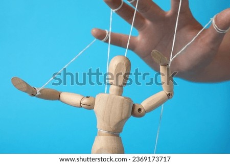 Woman pulling strings of puppet on light blue background, closeup