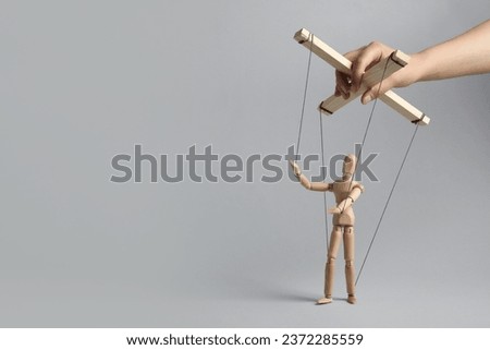Woman pulling strings of puppet on light grey background, closeup. Space for text