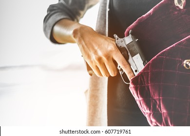 Woman pulls a gun from her swanky purse. Conceal carry weapon for protection themselves concept. Selective focus to gun.