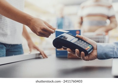 Woman purchasing food at the supermarket and paying with a credit card, the cashier is holding the POS terminal, hands close up
