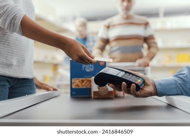 Woman purchasing food at the supermarket and paying with a credit card, the cashier is holding the POS terminal, hands close up - Powered by Shutterstock