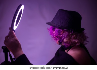 
Woman In Purple Hair Fedora Hat With Invisible Face Holding Round Shot Light In Her Hand.