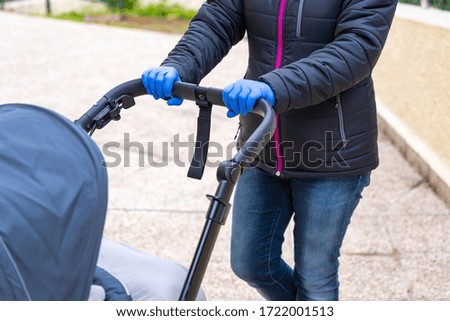 Woman pushing a baby carriage wearing nitrile medical gloves for protection