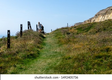 A Woman Pushing A Baby Stroller Up A Hill In Summer At Newhaven Beach In East Sussex, England