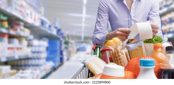 Woman pushing a cart and checking a grocery receipt, grocery shopping and expenses concept - Shutterstock ID 2125899800