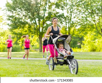 Woman pushing her little girl in a toddler while running outside with friends - Powered by Shutterstock