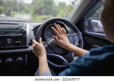 Woman pushing horn while driving sitting of a steering wheel press car, honking sound to warn other people in traffic concept. - Shutterstock ID 2221670777