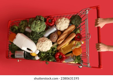 Woman pushing shopping cart full of food on red background