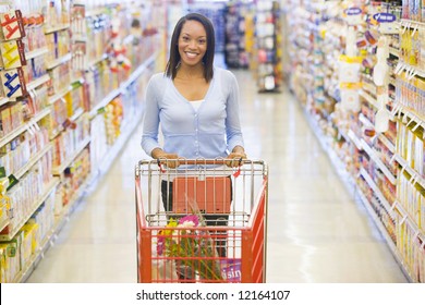 Woman Pushing Trolley Along Aisle In Supermarket