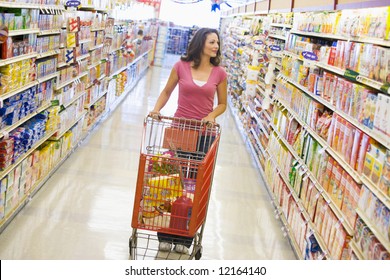 Woman Pushing Trolley Along Supermarket Grocery Aisle