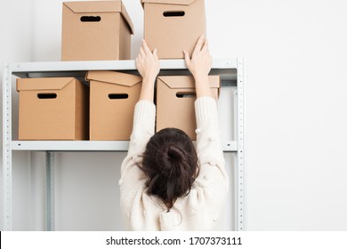 Woman put a cardboard box on a shelf of a rack in warehouse. Clean up and organize a pantry concept.  - Powered by Shutterstock