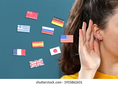 Woman put her hand to her ear, into which the flags of different countries fly. Close up. Blue background. The concept of learning foreign languages.