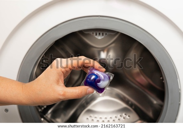 A\
woman put a liquid powder capsule into a washing machine with\
laundry, close-up. Gel for washing in the car. Colorful eco-gel for\
washing in capsules. Washing clothes. Purity\
concept