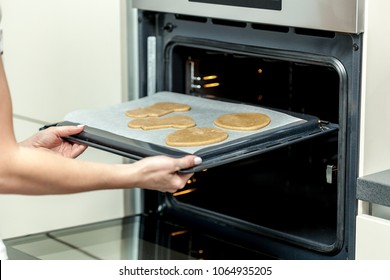 Woman put raw dough in oven in kitchen closeup. Cooking time.