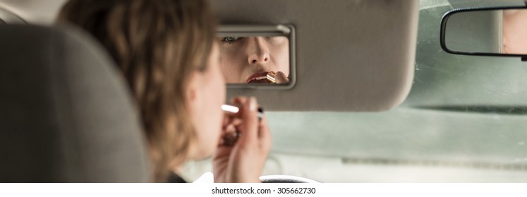 Woman is puting the lipstick on during driving - Powered by Shutterstock