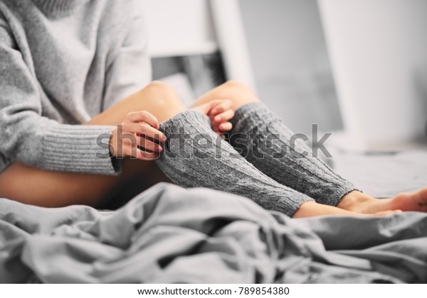 Woman puting on leg warmers while sitting on the\
bed in the morning.
