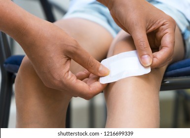 Woman puts adhesive bandage on child knee.