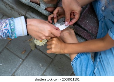 Woman Puts Adhesive Bandage On Child Foot. Mother Applying Bandaid To Daughter Outdoors