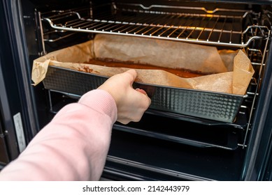 The woman puts the baking tray with the raw dough for the pie in the oven.
