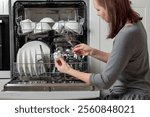 A woman puts a ball of aluminum foil into the dishwasher, cost-effective, environmentally friendly, and highly effective hack, the secret to sparkling silverware, spotless glassware and cutlery