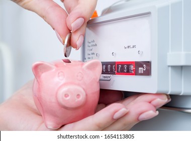 Woman Puts Coin In Piggy Bank Near A Gas Meter. Saving Natural Gas And Energy Efficiency At Home, Concept Image. 