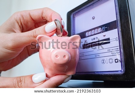 Woman puts coin in piggy bank near a electricity meter. Electricity consumption, cost of utilities and saving concept
