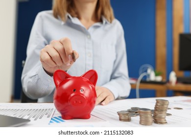 A Woman Puts A Coin In A Red Piggy Bank
