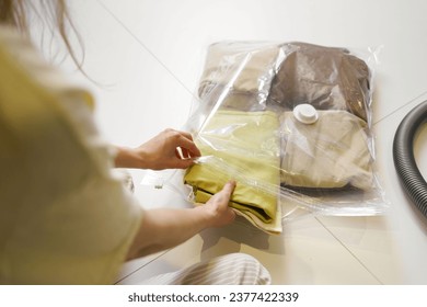 A woman puts compactly folded clothes in a transparent vacuum bag for seasonal storage in the closet. Hermetic bag for clothes concept - Powered by Shutterstock