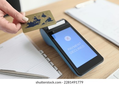 Woman puts credit card to terminal trying to pay for services online. Payment declined due to technical error. Device on wooden table in office closeup