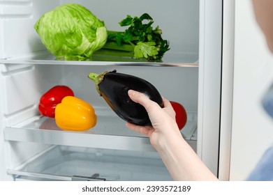 A woman puts an eggplant in the refrigerator. Fresh Vegetables lying on the shelf in the fridge. - Powered by Shutterstock