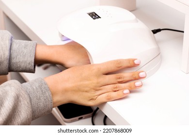 Woman puts hand with fresh beautiful pink modern gel polish manicure into led uv lamp for curing top cover of nailpolish. Process of drying gel on nails, close up. Beauty and self care
