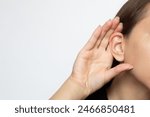 A woman puts her hand to her ear and listens, isolated on a white background with copy space. Hearing problems, ear diseases, noise. Concept of testing and hearing loss, audiometry