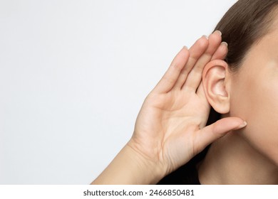 A woman puts her hand to her ear and listens, isolated on a white background with copy space. Hearing problems, ear diseases, noise. Concept of testing and hearing loss, audiometry