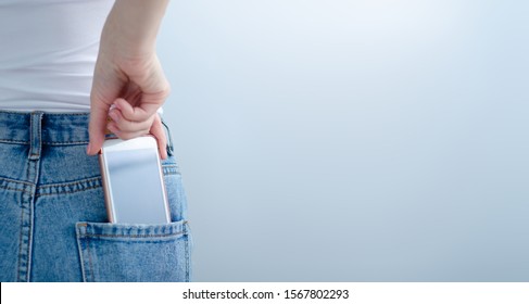 Woman puts mobile phone in jeans pocket on gray light background. Isolation, space for text