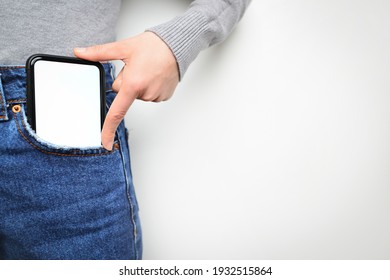 Woman puts mobile phone in jeans pocket on gray light background. Isolation, space for text. 