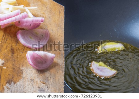 Woman puts slicing of red onion in hot oil for cooking curry fish