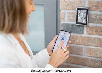 Woman puts the smart phone to the electronic reader to access the apartment or office. Cell with running mobile secure application - Shutterstock ID 2032700393