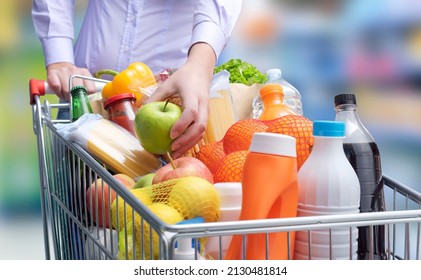 Woman putting an apple in a full shopping cart, grocery shopping concept