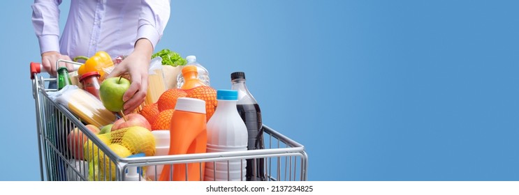 Woman Putting An Apple In A Full Shopping Cart, Grocery Shopping Concept