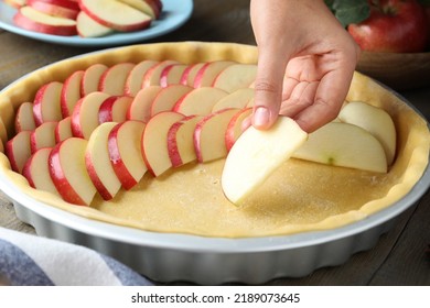 Woman putting apple slices into dish with raw dough at wooden table, closeup. Baking pie